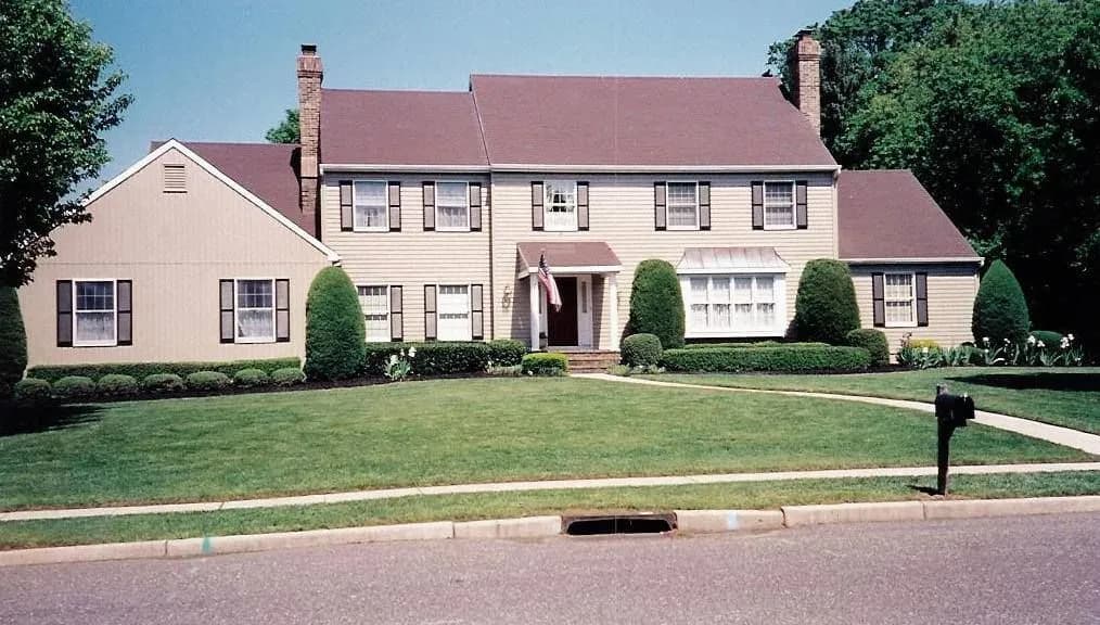 This is an image from Cherry Hill Painting in New Jersey. It shows a classic colonial-style home with white siding and dark shutters, freshly painted for a polished look.
