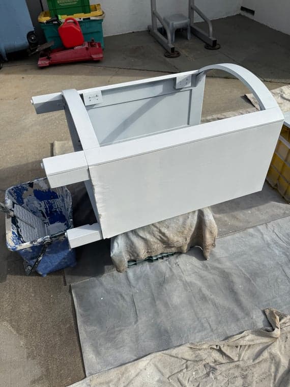 Metal frame with a fresh coat of light gray paint, supported on a covered work area.