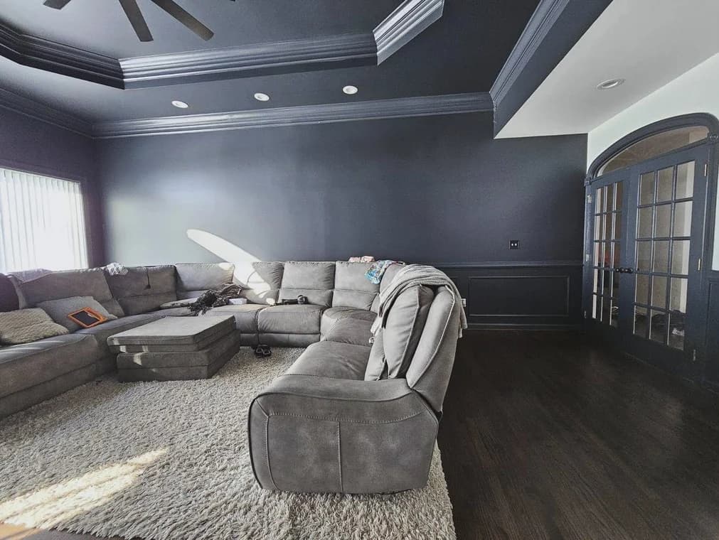 This is an image from CAZ Paintz LLC, located in New York. The living room shows dark navy walls, matching trim and ceiling accents, French doors, and a large sectional sofa.