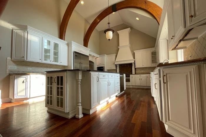 Cabinet painting project by Fulton Revivals in Chicago, IL. The image shows a large kitchen with white cabinets, arched openings, wood floors, and pendant lights.