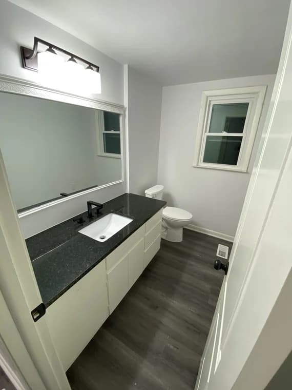 Interior painting project by Raleigh Paint & Improvement, LLC in Raleigh, NC. The image shows a bathroom with gray walls, white trim, and a black vanity top.