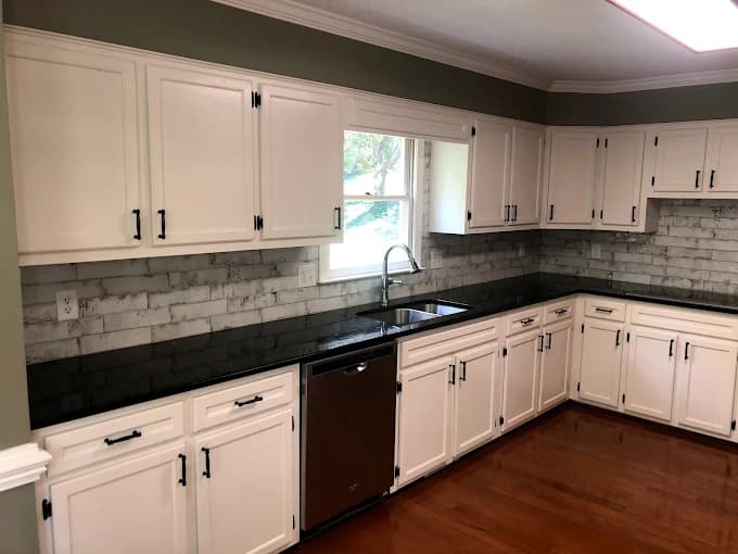 Cabinet painting project by Still Perfection Painting Co. in Belews Creek, North Carolina. The image shows white cabinets, dark counters, and tile backsplash.