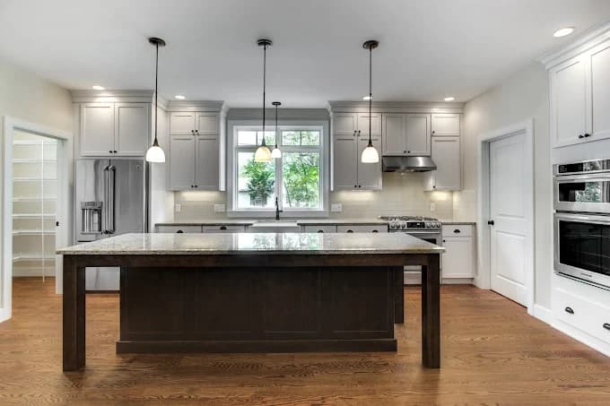 This is an image from DiNapoli Painting, located in Massachusetts. The photo shows a modern kitchen with freshly painted white cabinets, a large dark wood island, stainless steel appliances, and pendant lighting.