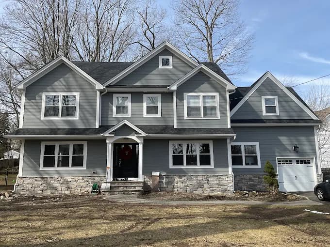 This is an image from Precision Painting NY, located in New York. The image shows a completed exterior painting project on a large gray two-story home with white trim and a stone foundation.