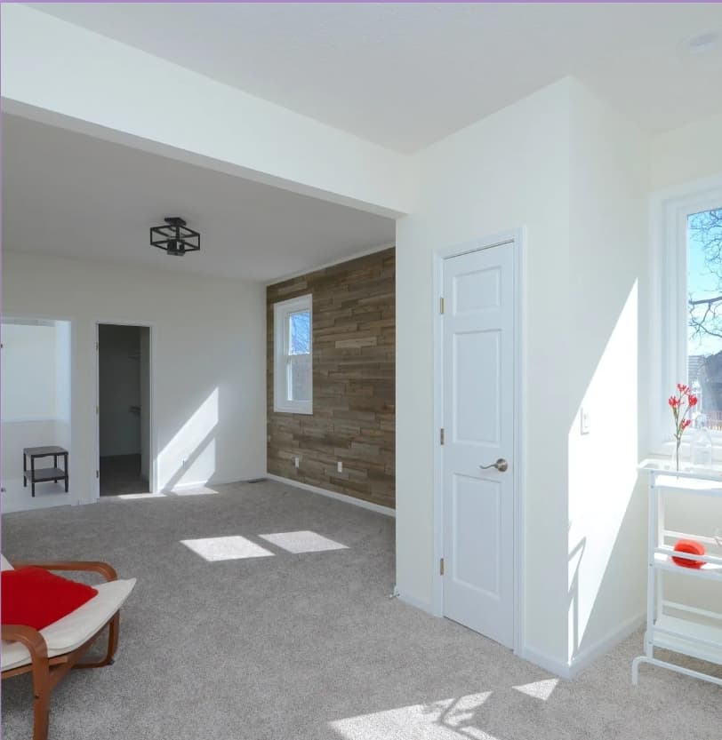 This is an image from Home Pros Painting And Home Repairs. The image is a bright interior room in Shawnee Mission KS with freshly painted white walls, new carpet, and a wood-accent feature wall.