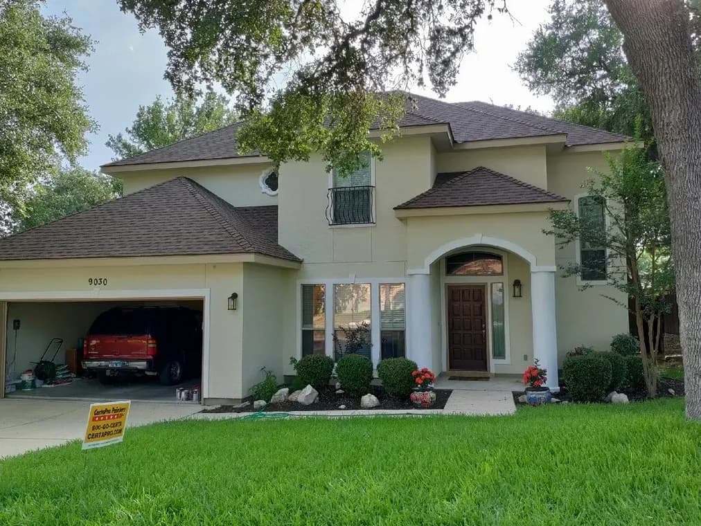 "This is an image from CertaPro Painters of NW San Antonio, located in Texas. The exterior view shows a two-story stucco home with a dark brown roof, white columns, and a landscaped yard."