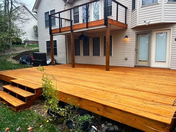 This is an image from Quick Painting LLC, located in Kentucky. The image shows a freshly stained wooden backyard deck with wide steps, clean railing lines, and a natural wood finish attached to a residential home.