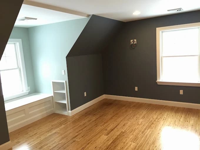This is an image from Firefly Painting Inc, located in Colorado. The room shows contrasting painted walls in soft blue and charcoal gray with bamboo flooring and a built-in bench by the window.