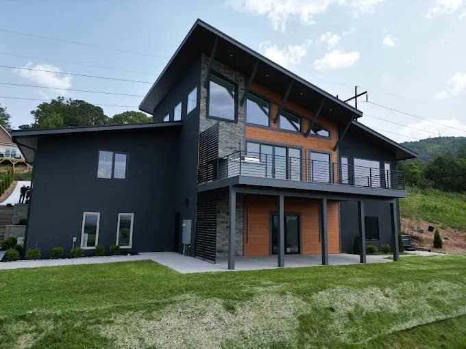 Exterior painting project by JV Painting Services in Hendersonville, NC. The image shows a dark modern home with wood accents, balconies, and a green lawn.