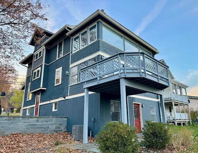 This is an image from Joseph Rivers Painting, located in Ohio. The image shows a multi-level blue house with a raised deck, large windows, and surrounding autumn landscaping.
