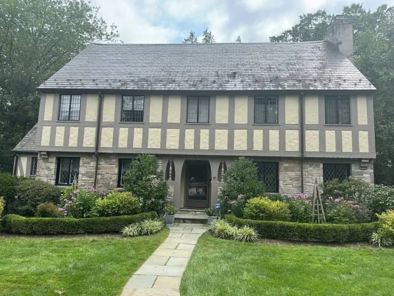 This is an image from Pier Painting Services, located in NY. The exterior photo shows a Tudor-style home with repainted trim and siding surrounded by landscaped greenery.