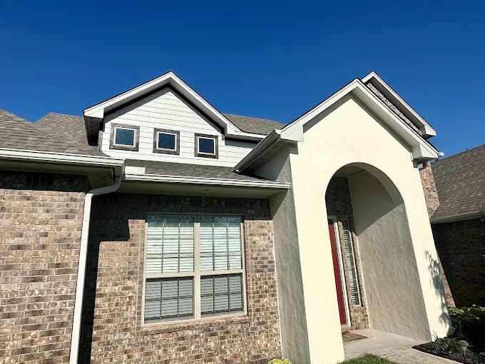 This is an image from Whitehead Brothers Painting, located in Oklahoma. The exterior photo shows a brick home with freshly painted light beige stucco accents and trim, highlighting the entryway and upper gables.