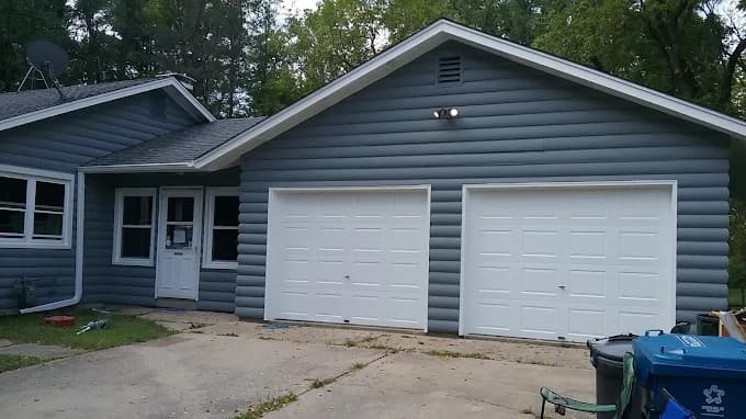 Exterior painting project by DIP Coatings in Troutman, NC. The image shows a gray garage with white doors, blue side entry, driveway, and trees.