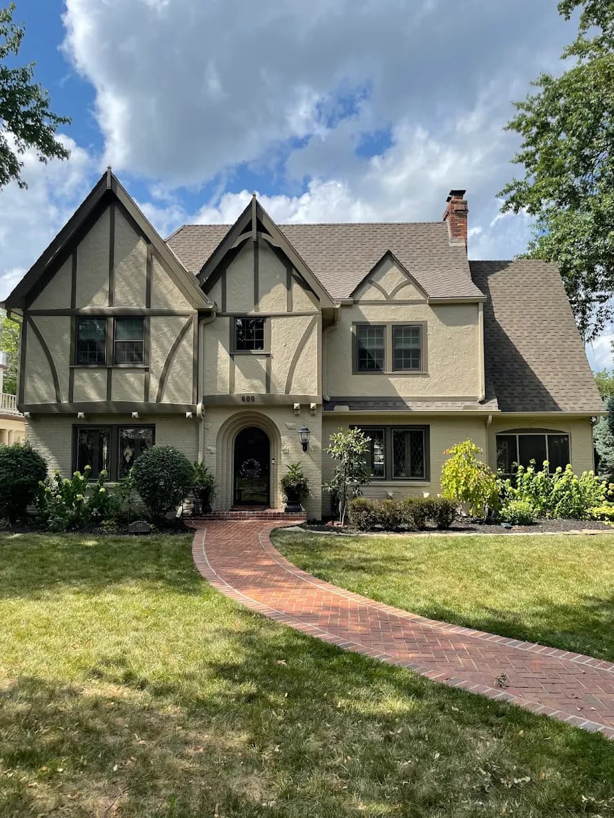 This is an image from Greg Baker Painting. The image shows an exterior Tudor-style home in Kansas City KS with textured stucco, dark trim accents, and a freshly painted facade.