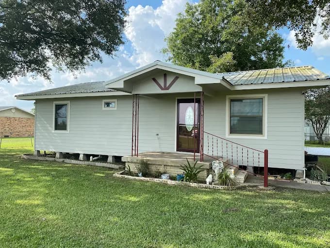 This is an image from 360 Painting of Lafayette, located in Louisiana. The photo shows a freshly painted light beige single-story home with white trim, a red front railing, and a well-kept green lawn under a partly cloudy sky.