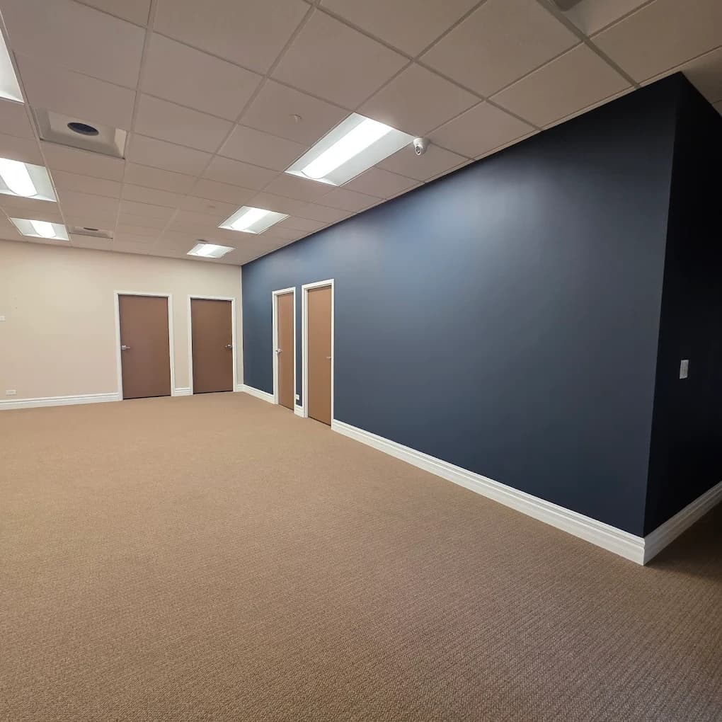 This is an image from Angel the Painter Inc., located in Illinois. The image shows a commercial office interior with dark blue accent walls, beige carpeting, suspended ceiling lighting, and multiple office doorways.