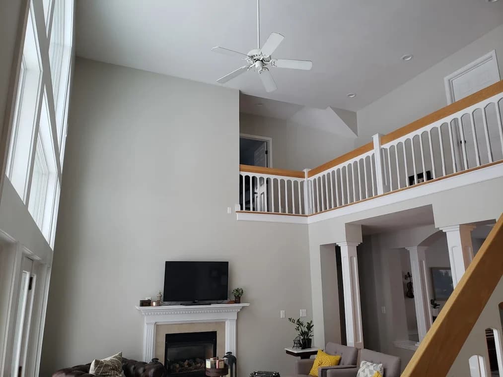 This is an image from Braun's Painting, LLC, located in New York. The interior photo shows a large living room with tall painted walls, a white fireplace, and an upper balcony railing
