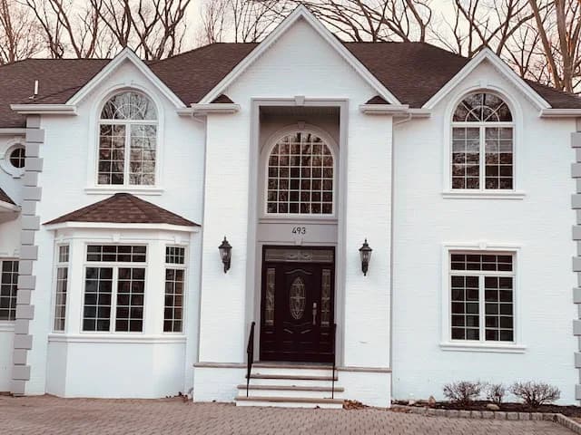 This is an image from Spectrum Painting, located in New Jersey. The photo shows a freshly painted two-story home exterior in crisp white with dark trim and a black front door.