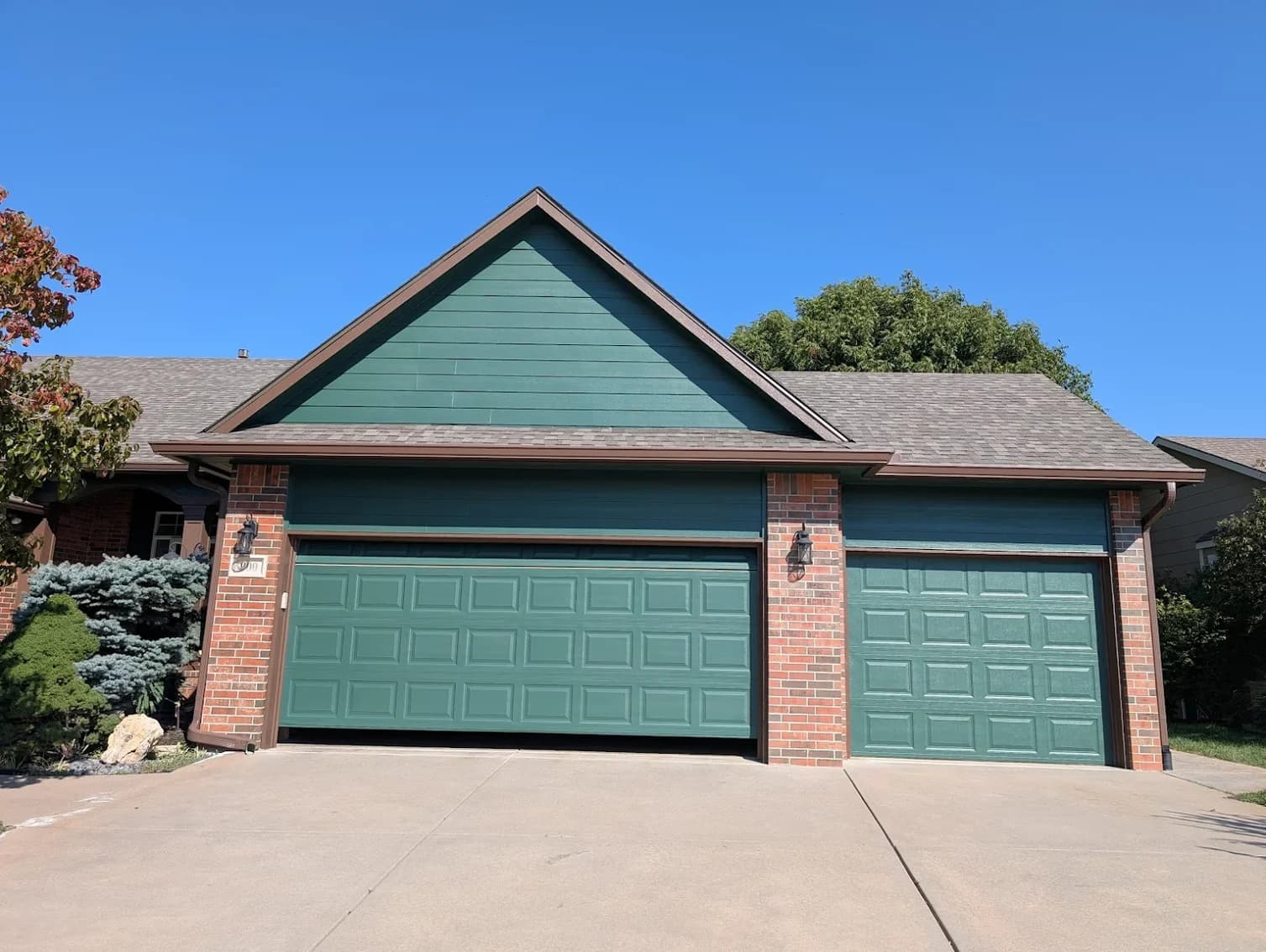 This is an image from 360 Painting of Wichita. The image shows a home exterior with green siding, matching green garage doors, and brick accents.
