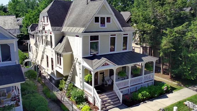This is an image from JT’s Painting 518 LLC, located in New York. The image shows a freshly painted multi-story home exterior with light siding, dark roof accents, and detailed trim work.