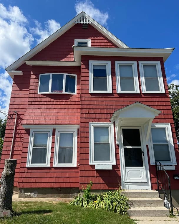 This is an image from EVM Home Improvement & Painting, located in Massachusetts. The photo shows a two-story home with freshly painted red siding and white trim around the windows and entryway.
