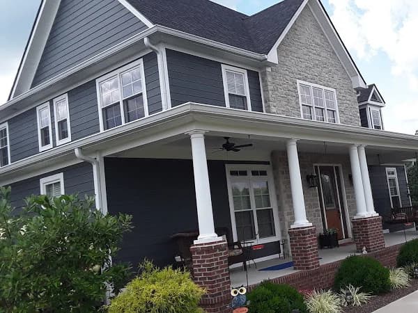This is an image from Big J Painting LLC, located in Kentucky. The photo shows a two-story home with dark gray siding, white trim, and a stone accent facade, highlighting detailed exterior painting and finish work.
