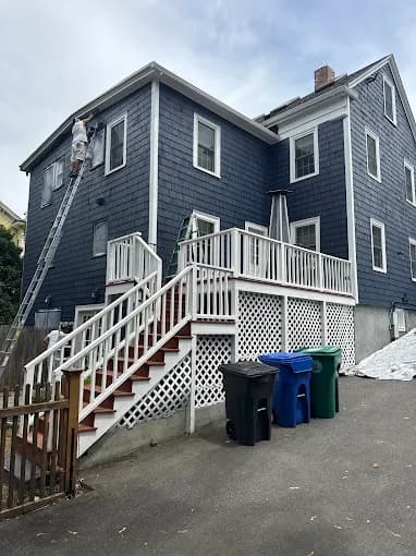 This is an image from ProTEK Painters, located in Massachusetts. It displays a two-story home with navy blue siding, crisp white trim, and double garage doors.