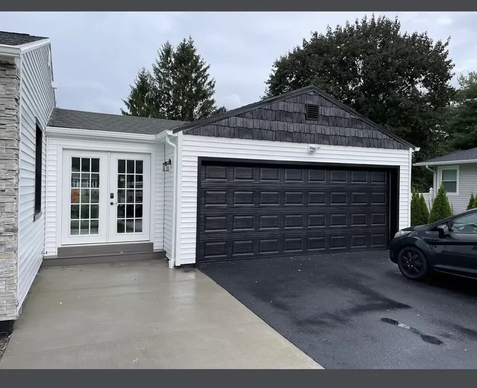 This is an image from R&R Painting & Concrete Coatings, located in New York. The photo shows a freshly painted black garage door and white exterior siding on a residential home.