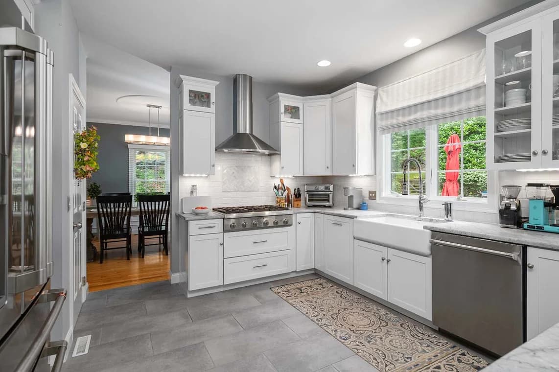 This is an image from AH Painting Services, located in Massachusetts. The photo showcases a modern kitchen with freshly painted white cabinetry, light gray walls, and a sleek design that highlights the company’s professional interior painting services.