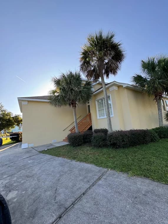 This is an image from Falcon Remodeling Express LLC company, located in Fort Walton Beach, FL. The image is a freshly painted yellow exterior of a Florida-style home with palm trees, white trim, and clean landscaping under a clear blue sky