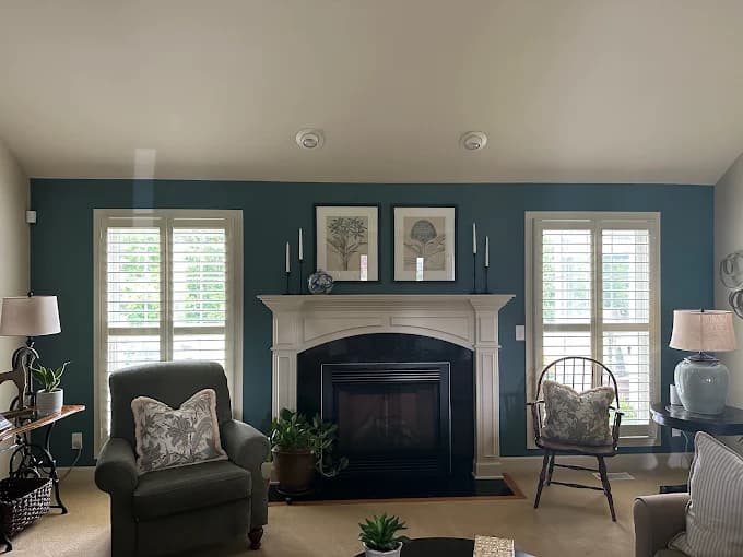 This is an image from Advantage Paint Services, located in New York. The image shows a living room with teal painted walls, a white fireplace mantel, plantation shutters, and coordinated furniture accents.