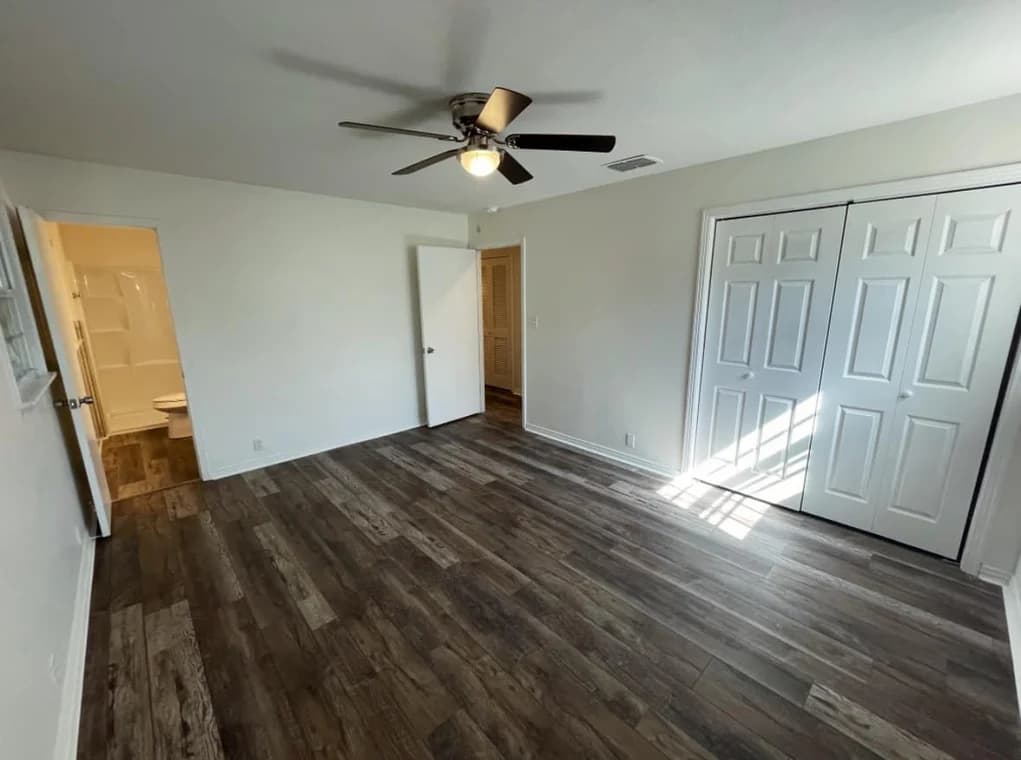This is an image from TopBrush Painting company, located in Altamonte Springs, FL. The image is a freshly painted bedroom with white walls, dark wood vinyl flooring, ceiling fan, and natural light from window near double-door closet