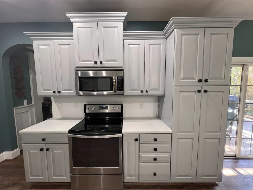 Cabinet painting project by Icarus Pro Painters in Charlotte, NC. The image shows white cabinets, dark appliances, and arched doorway.