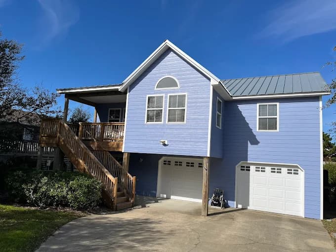 Exterior painting project by Kitty Hawk Painting in Kitty Hawk, NC. The image shows a light blue home with white trim, garage doors, and stairs.