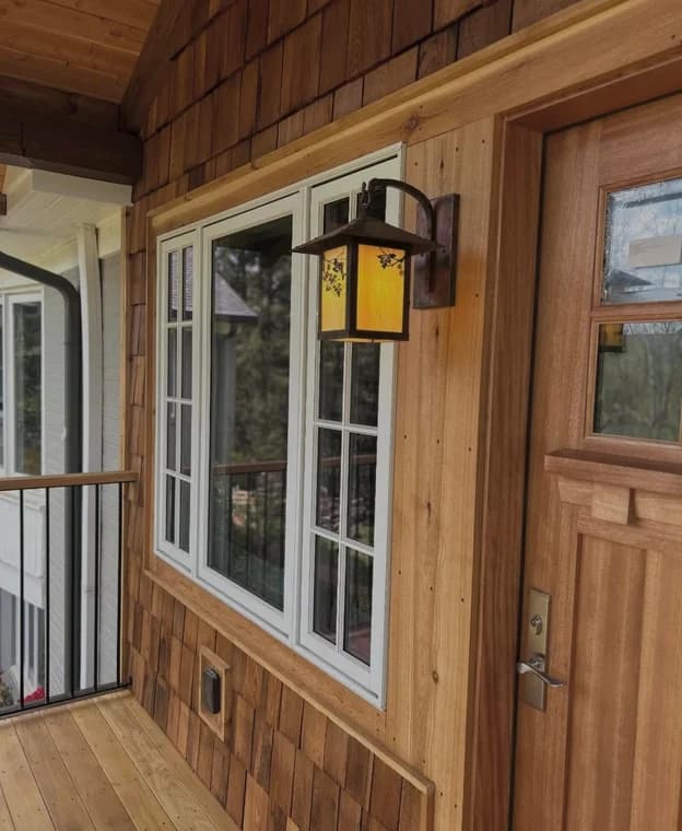 Exterior staining project by Passion Painters in Swannanoa, NC. The image shows wood shingles, a wood door, white window trim, and an amber wall lantern.