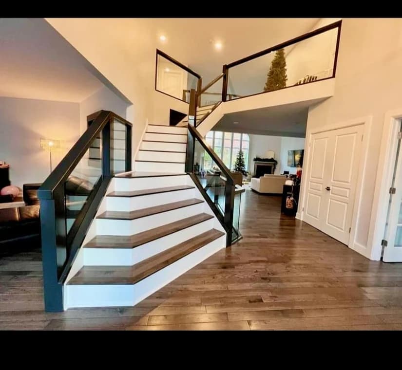 This is an image from Level Up Painting, located in New York. The interior photo shows a modern staircase with dark-stained treads, white risers, and glass panel railings in a bright open living space.