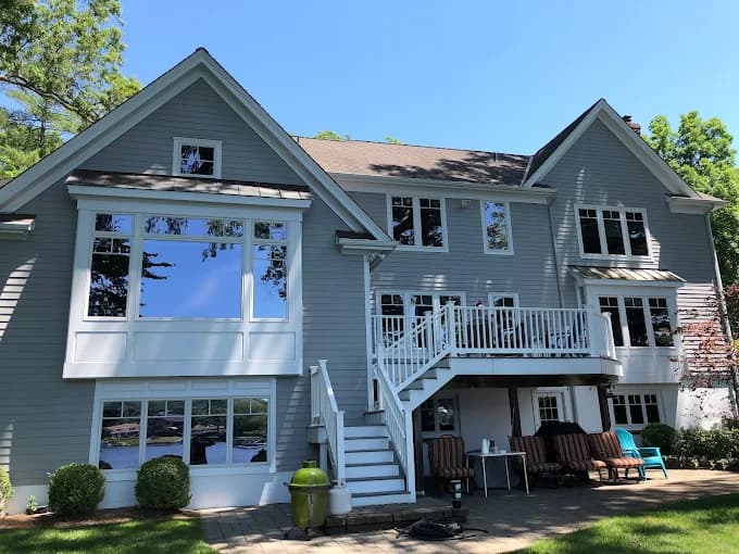 This is an image from Spectrum Painting, located in New Jersey. The photo shows a large gray-painted home with white trim, multiple windows, and a white deck overlooking the backyard.