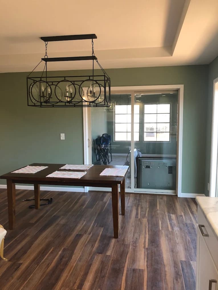 Interior painting project by Neff Paints in Warren, Illinois. The image shows a dining space with sage green walls, dark flooring, and a wood table.