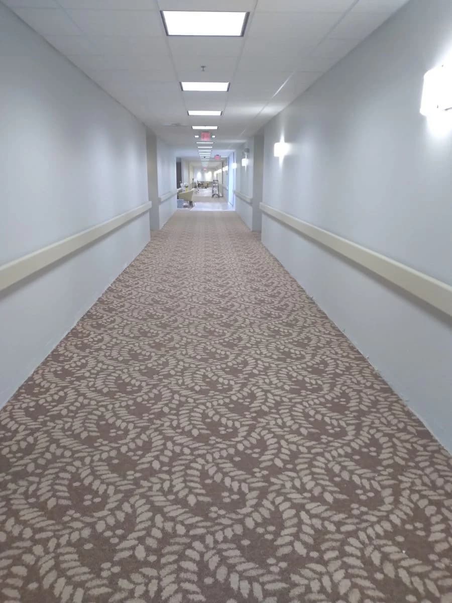 This is an image from CertaPro Painters of Wichita East KS. The image is a long commercial hallway in Wichita KS with fresh light-gray wall paint and patterned carpet.
