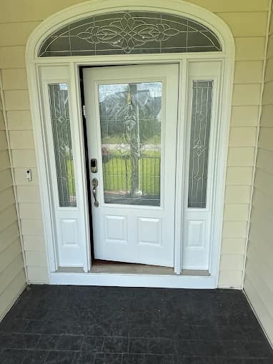 Exterior trim painting project by Garner's Painting Service in Fayetteville, North Carolina. The image shows a white front door, glass side panels, yellow siding, and entry mat.