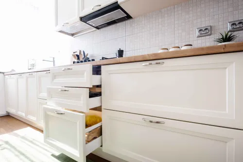 This is an image from The Woodlands Paint Doctor, located in Texas. The photo captures white shaker-style kitchen cabinets with drawers open, showing organized interior storage and a wood countertop.