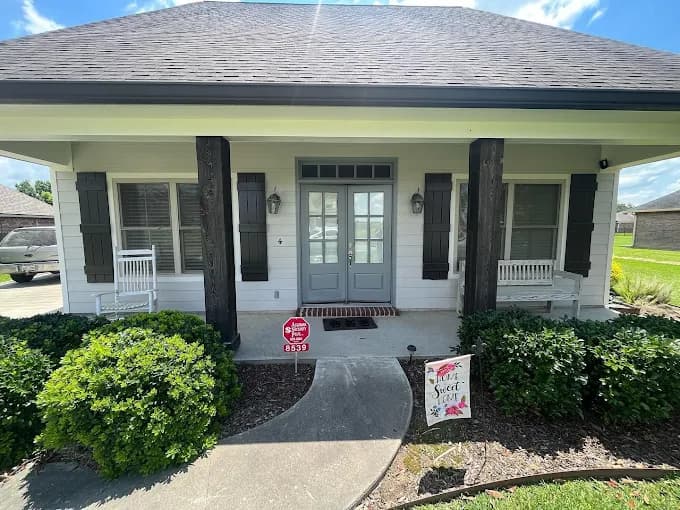 This is an image from Spell Painting, located in Louisiana. The photo shows a freshly painted home exterior with white siding, dark shutters and columns, and a light blue front door, giving the entryway a clean, modern look.