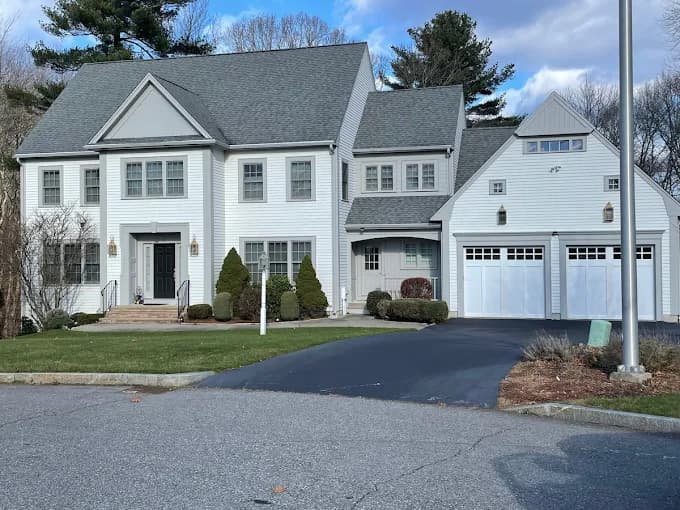This is an image from Aurora Exterior Painting Inc., located in Massachusetts. The photo shows a large colonial-style home with freshly painted white siding, gray roofing, and an attached garage, creating a bright and elegant exterior look.