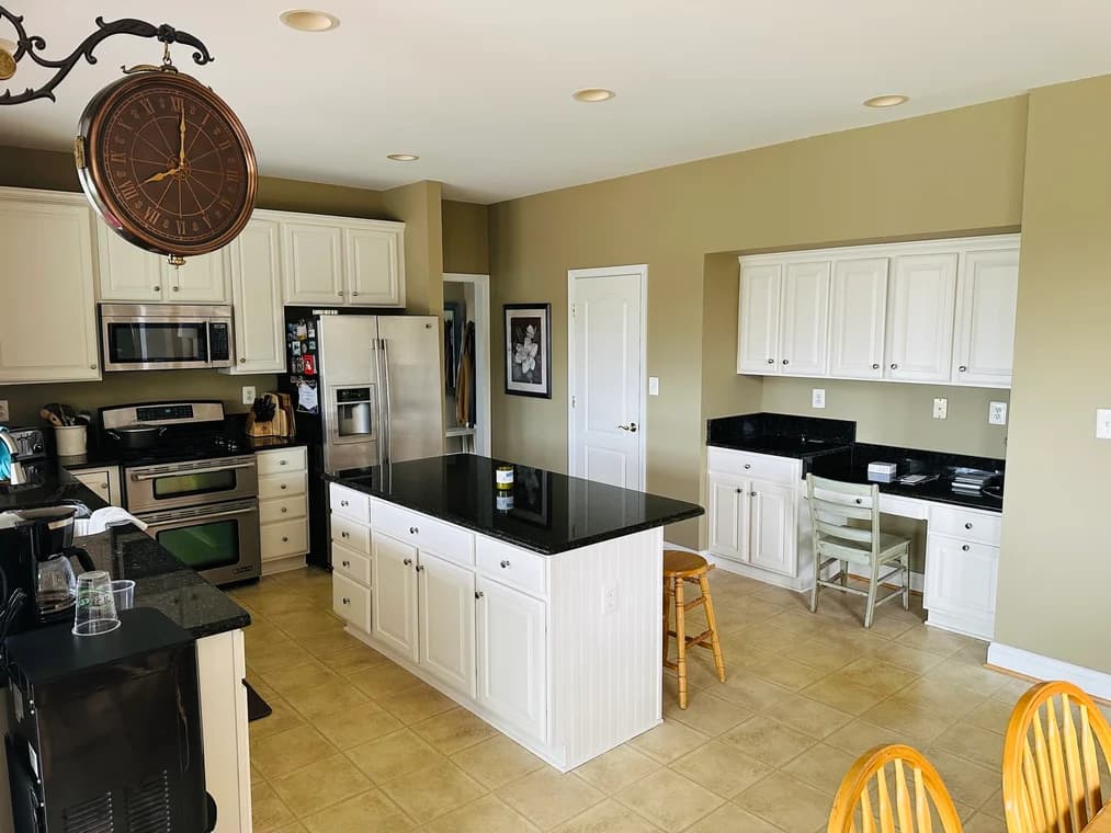 This is an image from Painting Contractors of MD, located in Maryland. The kitchen interior includes white cabinetry, black countertops, stainless steel appliances, and a center island under soft recessed lighting.