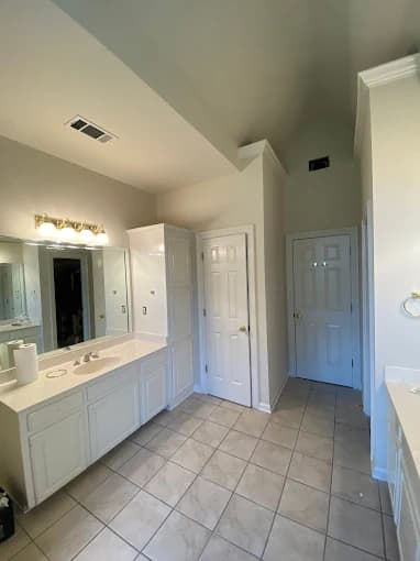 This is an image from Yeras Painting, located in Louisiana. The photo shows a bright, freshly painted bathroom with white cabinets, light beige walls, a large mirror, and tiled flooring under soft ceiling lighting.