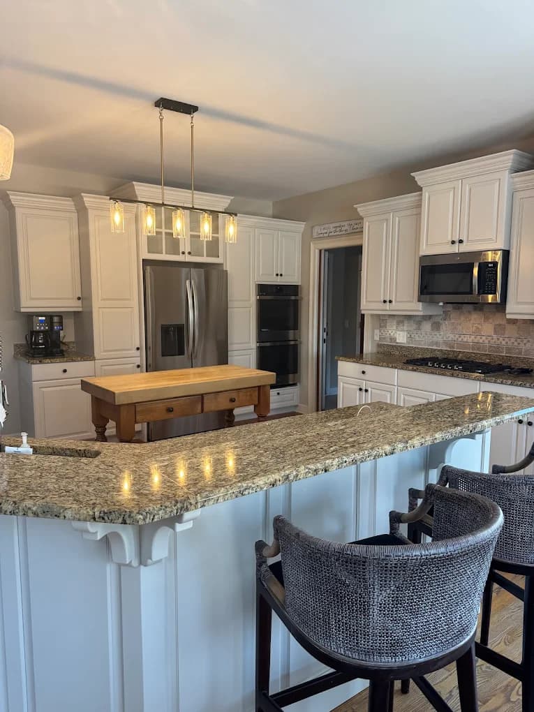 Cabinet painting project by Campos Painting in St. Charles, IL. The image shows a kitchen with white cabinets, granite counters, pendant lights, and stainless appliances.