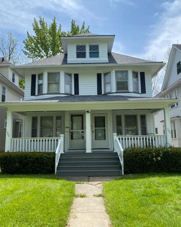 This is an image from Level Up Painting, located in New York. The exterior photo shows a white two-story home with black shutters and a covered front porch with gray steps and railings.