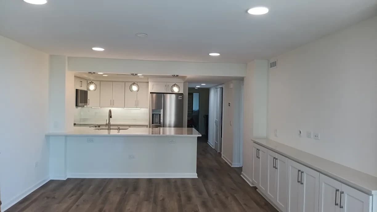 Interior painting project by Erazo's Painting LLC in Supply, NC. The image shows white walls, recessed lights, wood flooring, and a kitchen.