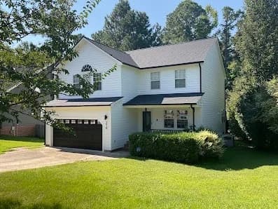 Exterior painting project by CertaPro Painters of Durham, NC in Durham, NC. The image shows a white two-story home with black shutters, a garage, and green lawn.