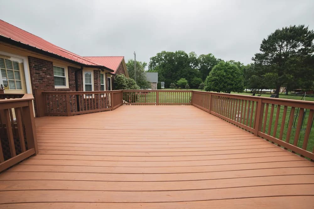 This is an image from Richard's Painting of Barnegat, located in New Jersey. It highlights a freshly painted wooden deck with a warm brown finish, attached to a brick home with views of a large backyard.